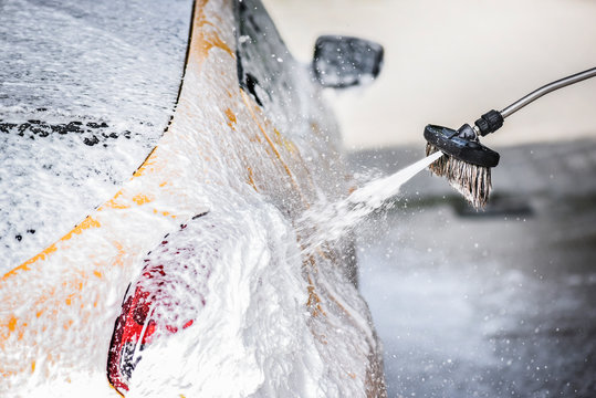 Car washing close up. Cleaning a car with foam brush and high preasure water.