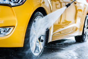 Man cleaning vehicle with high pressure water jet. Car wash details or close up.