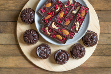 Healthy homemade recipe chocolate sticks with almonds, cashews and raspberries, and candies lie on a saucer. Round tasty sweets on a kitchen board on a wooden background. Copy space. Top view