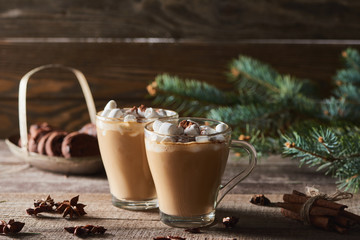 selective focus of cacao with marshmallow and cacao powder in mugs near pine branches, cinnamon and anise on wooden table