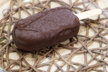 Fresh raw delicious vegan homemade popsicle on stick coated with chocolate glaze lay on wicker tablecloth. Top angle view. Close-up. Selective focus. Healthy meal. Copy space. Made from bananas