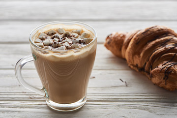 cacao with marshmallow in cup near croissant on white wooden table