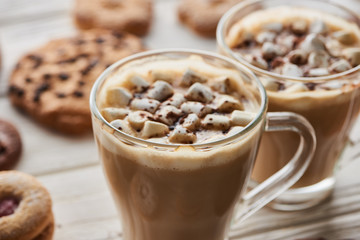 selective focus of cacao with marshmallow in mugs near cookies on white wooden table
