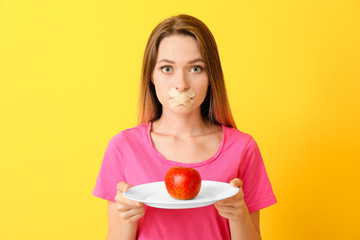 Woman with taped mouth and healthy apple on color background. Diet concept