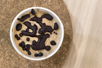 Top view healthy vegan sweet frozen dessert on round kitchen desk. Raw banana ice cream with coconut cream with natural chocolate droplets in a white paper cup on wicker tablecloth. Copy space