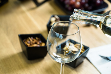 Pouring white wine into the glass against wooden table