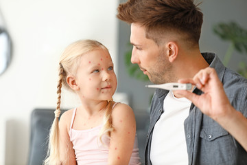 Man measuring temperature of his little daughter ill with chickenpox at home