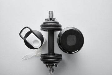 top view of spoon near protein, dumbbell and sports bottle on white