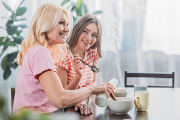 selective focus of cheerful mother and daughter sitting at kitchen table and having breakfast