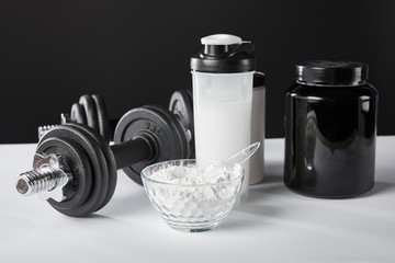 selective focus of bowl near dumbbells and sports bottle with protein shake on black