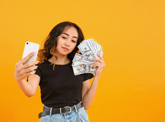 Asian woman with money taking selfie on color background