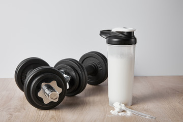 Fototapeta na wymiar spoon with protein powder near black dumbbells and sports bottle isolated on grey
