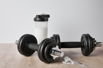 Obraz na płótnie Canvas spoon with protein powder near dumbbells and sports bottle isolated on grey