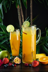 pineapple mango cocktail in a jug and glass on a dark background with fruits