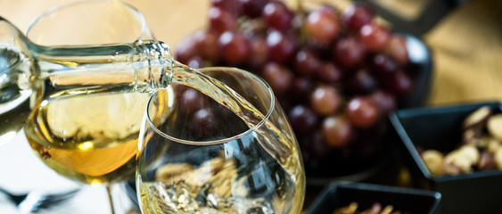 Pouring white wine into the glass against wooden table