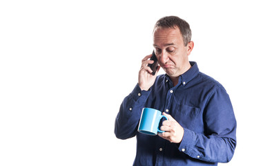 Man in casual blue shirt with blue cup of coffee on white background ignoring phone conversation