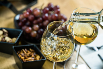 Pouring white wine into the glass against wooden table