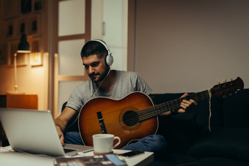 man playing guitar at his home. using on line lessons