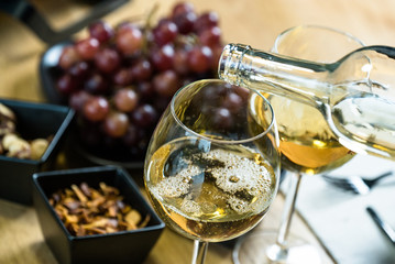 Pouring white wine into the glass against wooden table