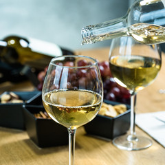 Pouring white wine into the glass against wooden table