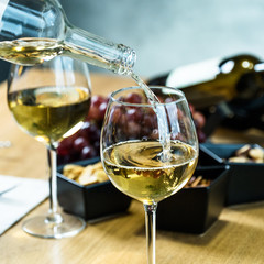 Pouring white wine into the glass against wooden table