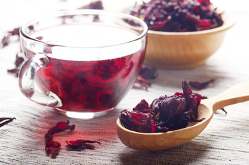 Closeup view at wooden bowl tea cup and spoon of dry hibiscus petals on linen cloth background