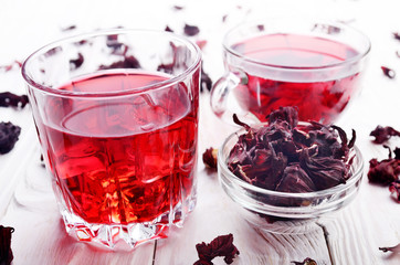 Closeup view at two tea cups with ice and dry hibiscus petals on white wooden table background