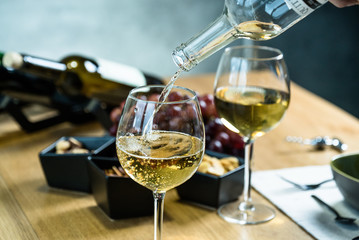 Pouring white wine into the glass against wooden table