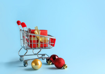 Small shopping cart with gift box on color background