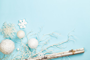Frost like christmas composition with snowy branches, birch sticks, white shiny spheres or balls and snow flakes over a light blue background. Flat lay, top view with copy space.