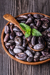 Whole dry cocoa beans in wooden bowl spoon on old rustic background.