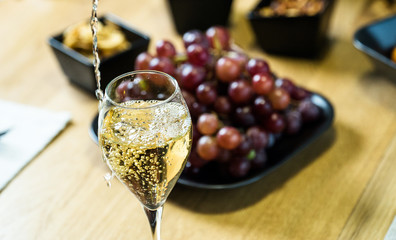 Pouring white wine into the glass against wooden table