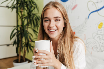 Fototapeta premium Cute girl in pajama at home on bed drinking coffee.