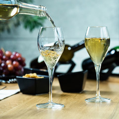 Pouring white wine into the glass against wooden table
