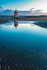 Naklejka premium Sunrise over the sea. The lighthouse of Lignano Sabbiadoro and the games of sand and colors. Italy