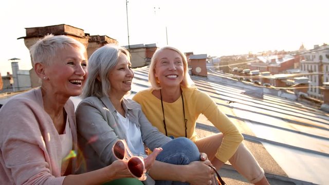 Group of three multiethnic middle-aged women sitting together on roof during daytime and chatting