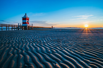 Sunrise over the sea. The lighthouse of Lignano Sabbiadoro and the games of sand and colors. Italy - 296550106