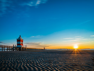 Sunrise over the sea. The lighthouse of Lignano Sabbiadoro and the games of sand and colors. Italy