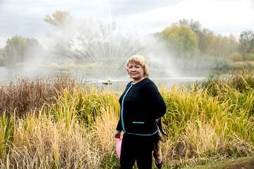 A woman stands on the background of a fountain spurting from a river in an autumn city park. © Vera