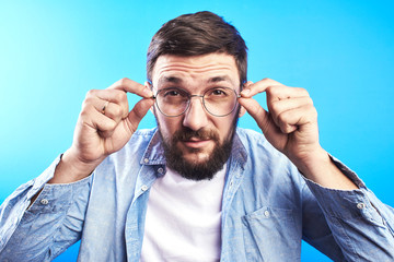 Handsome Caucasian bearded man with glasses squinting, trying to look closer isolated on blue...