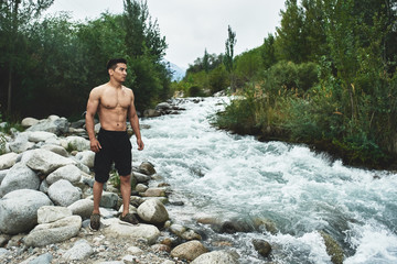 Kazakh muscular athlete man trains and exercises by the river in nature. Asian handsome does extreme fitness workout outdoors