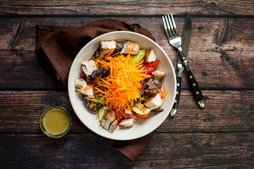 Salad with grilled chicken breast, carrot, red onion and roasted vegetables with dressing on dark rustic wooden table