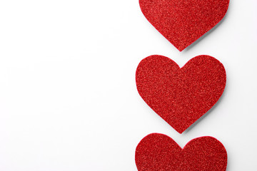 Red shiny paper hearts on white background, top view