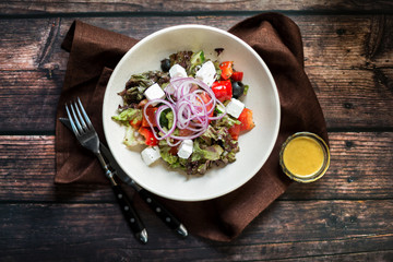 Greek salad with red onions, feta cheese, cherry tomatoes and olives on dark wooden table