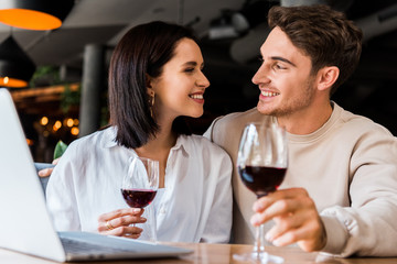 happy man and woman with glass of wine looking at each other near laptop