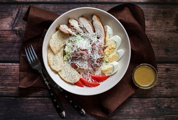 Caesar salad with grilled chicken with dressing on rustic wooden table