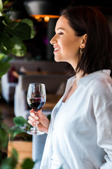 side view of cheerful woman holding glass with red wine