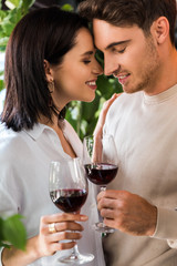 selective focus of happy man holding glass with red wine near beautiful girl