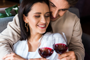 happy man holding glass with red wine near cheerful girl