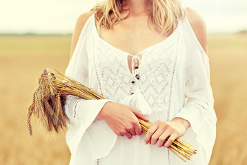 country, nature, summer holidays, vacation and people concept - close up of smiling young woman in white dress with spikelets on cereal field